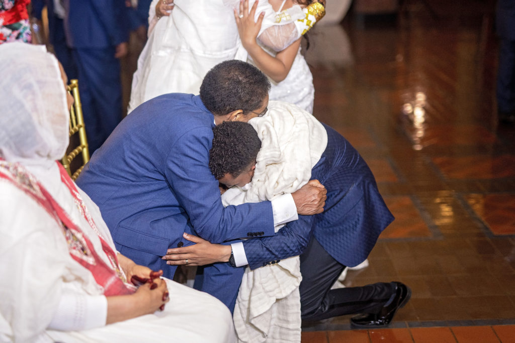Groom hugging feet of elders receiving a blessing for his marriage traditional ethiopian wedding minnesota