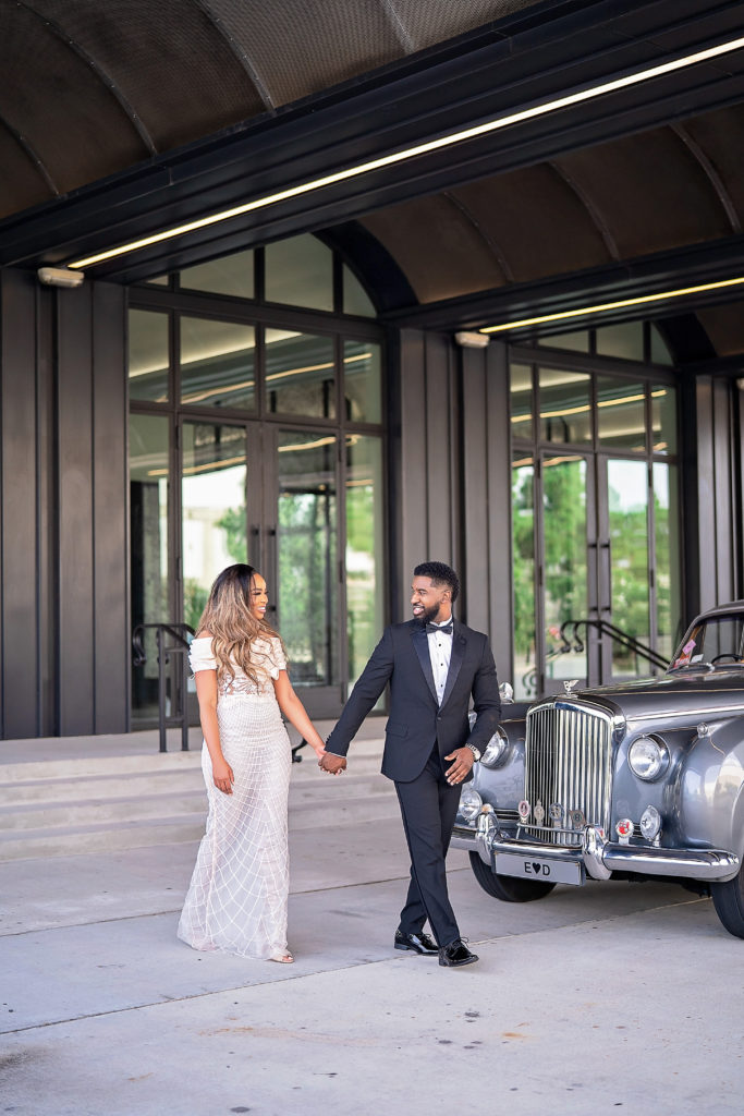 Retro Hollywood Glamor Engagement Session at The Revarie Houston with Black Couple walking outside venue in length cream gown and classic black tux