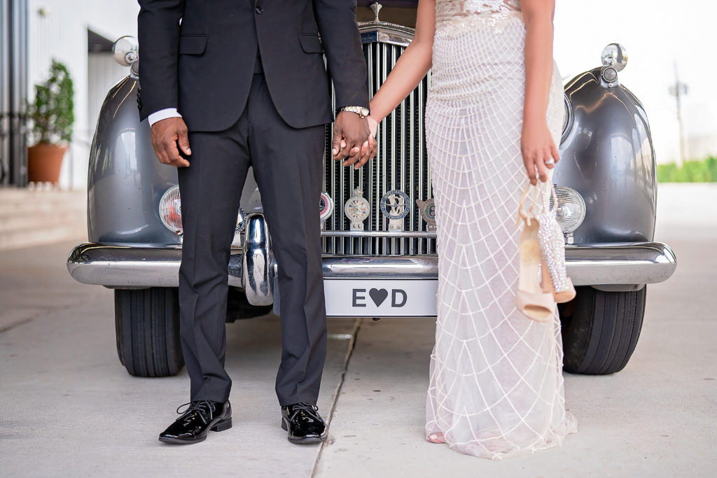 Retro Hollywood Glamor Engagement Session at The Revarie Houston with Black Couple holding hands in front of 1959 bentley in high end cream gown and classic black tux