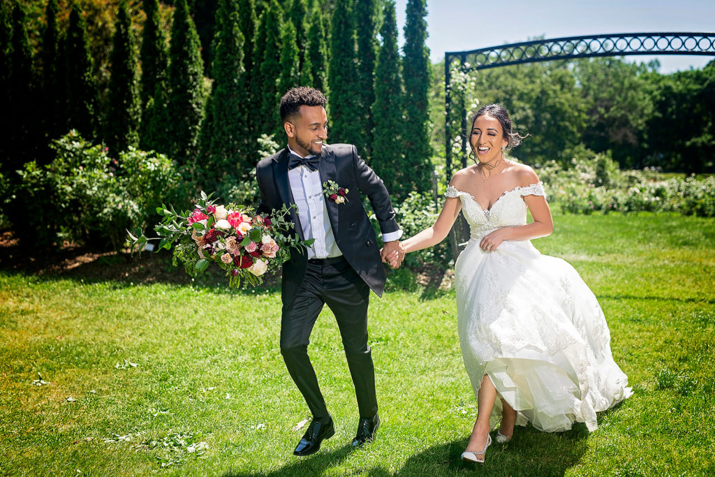 bride and groom playfully running in a garden
