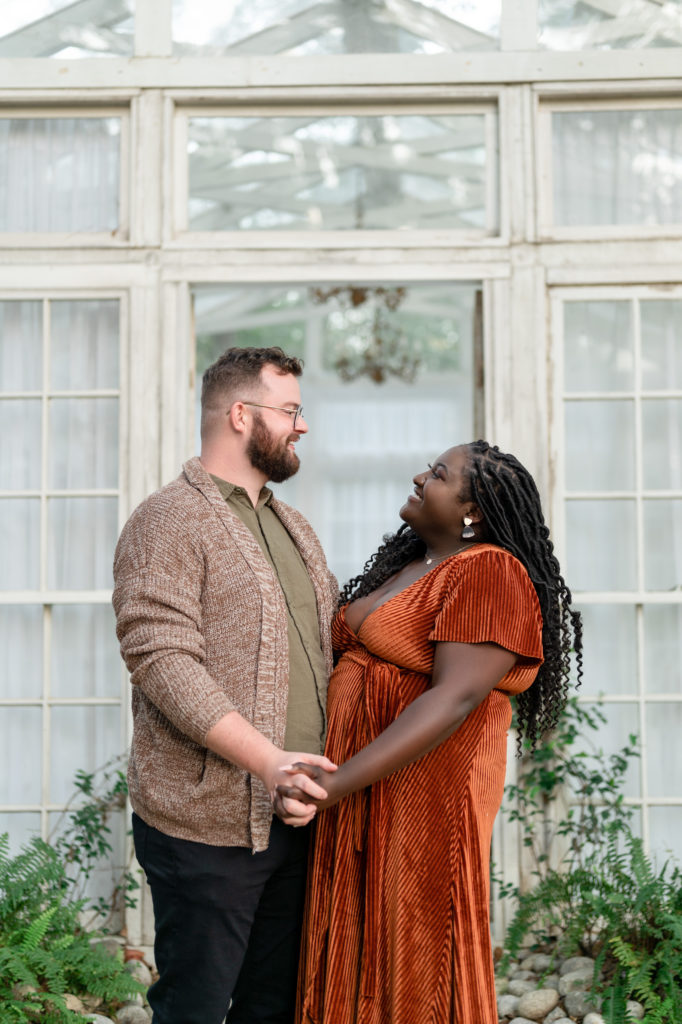 cute engaged couple pose outside a greenhouse staring into each other's eyes 