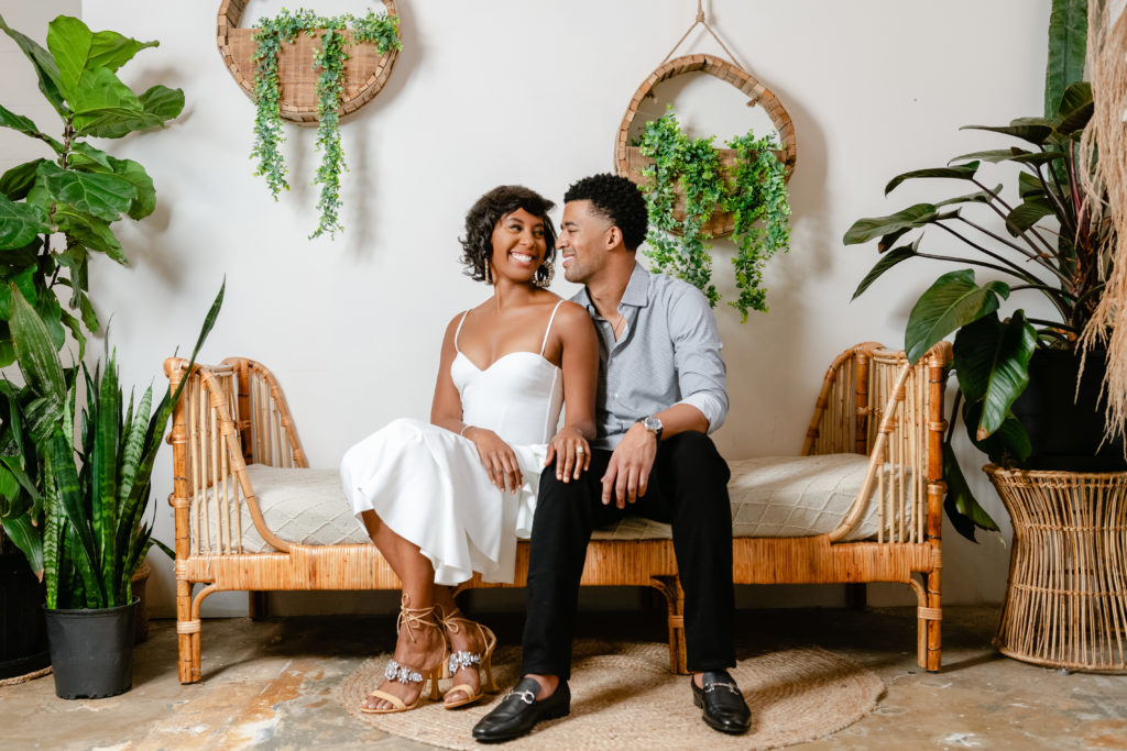 engagement photo session, sitting down poses, neutral background, indoor photoshoot, greenery, white dress, men engagement outfit