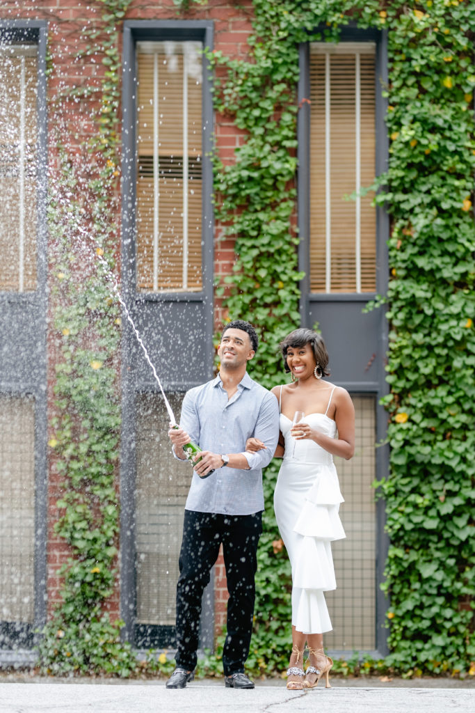 Outdoor photoshoot, outdoor engagement session, couple posing, white dress engagement, greenery backdrop, champagne popping,